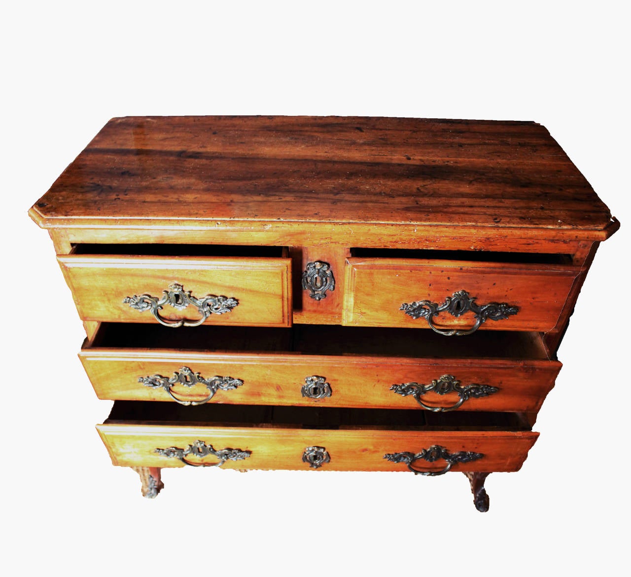 Rustic feminine French walnut commode on raised legs that are hand carved. Features four drawers, original hand forged bronze pulls and bow motif escutcheons.