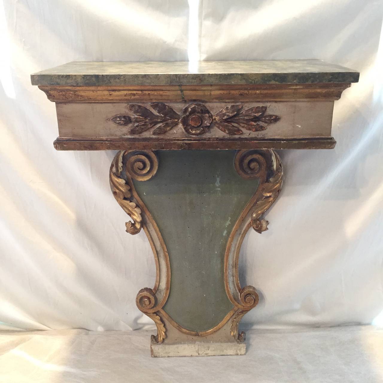 Small console table with gilt carving detail, hand-painted top made to look like marble. Hues of greens, whites, golds and greys throughout. Could work as a small sink pedestal or under a narrow mirror.