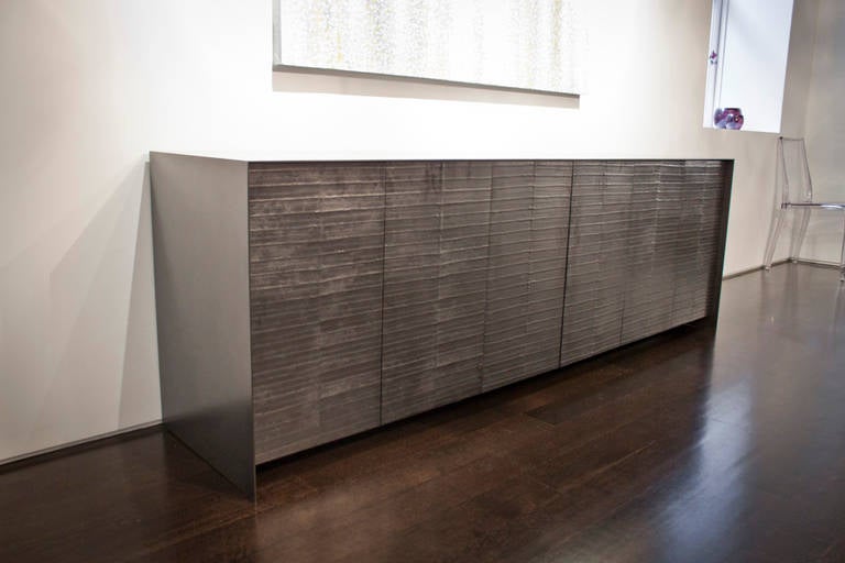 This credenza is the quintessence of rarefied and subtle elegance. Six front panels are adorned with graphite eel skin, and enhanced by a steel frame in polished antique black patina. A dynamic statement piece, the credenza opens up to reveal