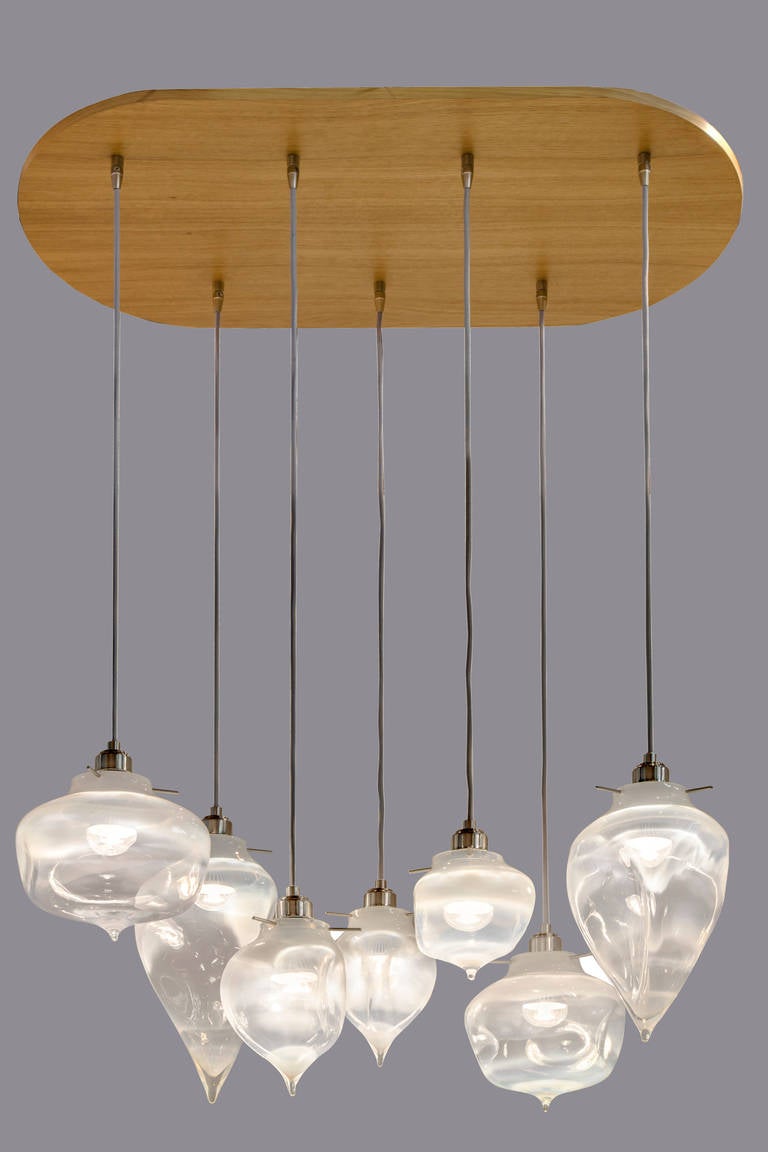 Handblown pendants suspended by chords undulate like molten glass in the sparkle of Edison-style bulbs. The wood canopy lends an industrially chic flair to this chandelier, which casts a warm glow in any room.

We specialize in custom