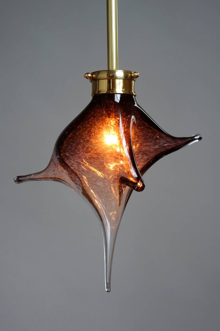 A handblown glass pendant is resplendent when turned out in a shell-inspired shape, which gracefully stretches from a single brass column that glows with a shiny finish. Hang alone or in a group for dramatic impact. Uses one 40 watt chandelier