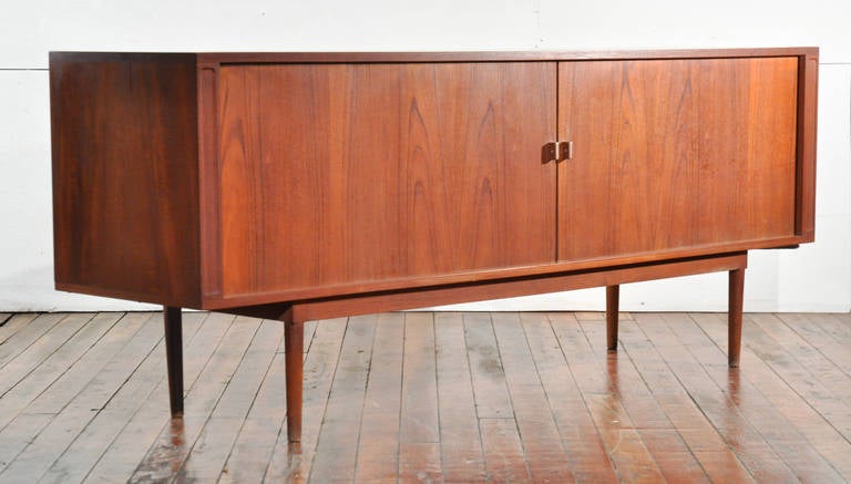 Danish, circa 1960s, teak. This tambour door sideboard features split cabinet shelves to each side and a column of drawers in the middle. Really wonderful piece, it exemplifies the Danish Modern furniture movement. Each door is accented with a metal