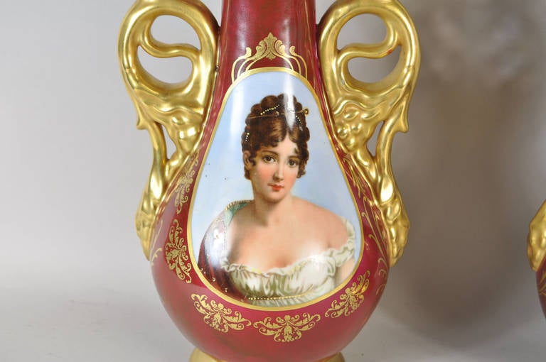 A beautiful pair of hand painted porcelain double handled urns.  The pieces are marked to the bottom and are in very good condition. Each features a detailed image of women with gilt paint along the base, rim, and handles.

Worrell Smith Gallery