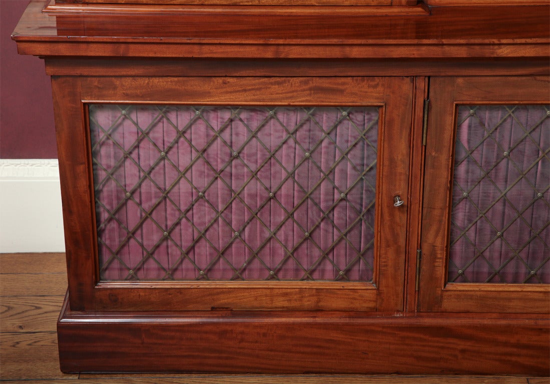 The cornice of reverse breakfront form over an egg and dart edge and roundel mounted frieze, above glazed brass grille-mounted doors opening to adjustable shelves; the lower part with glazed brass grille-mounted and silk-lined doors opening to