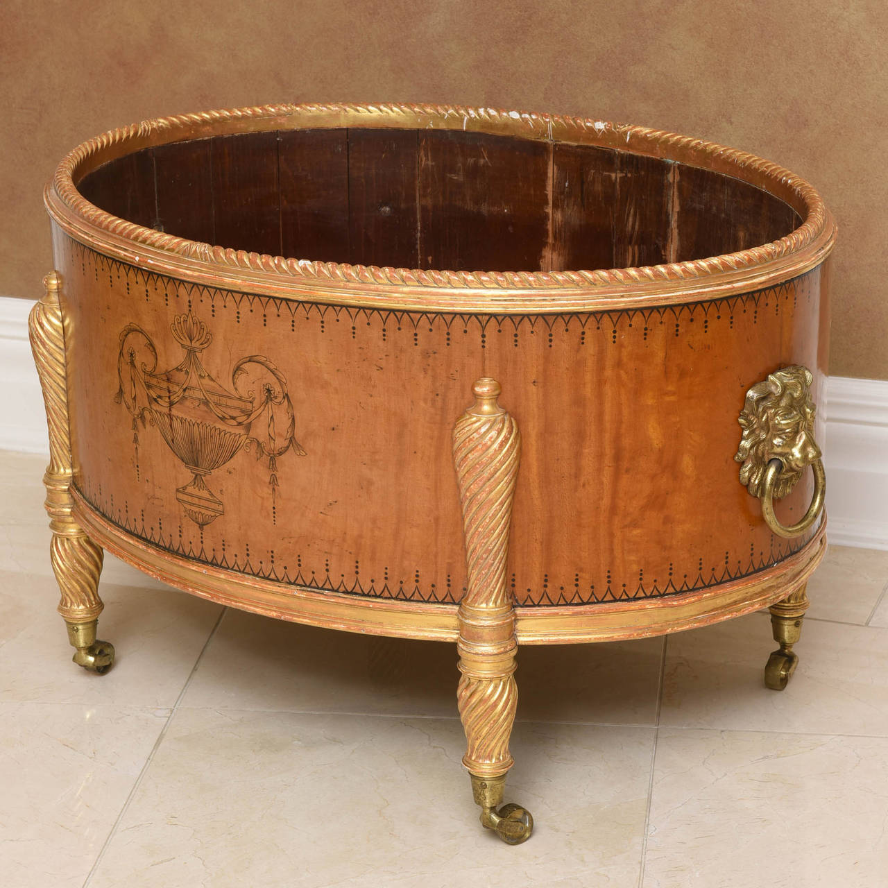Of oval form with gilt gadrooned edge over a finely etched classical urn; with gilt-metal lion mask handles to the sides; raised on gilt spiral-fluted legs terminating in brass caps and casters; retaining aluminum lining.

Spectacular filled with