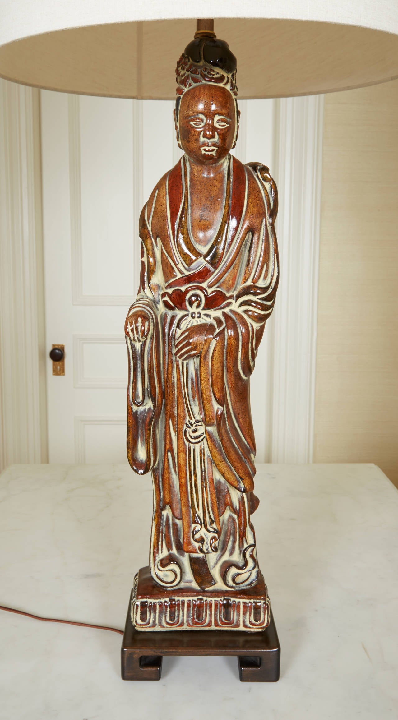 Comprising a pair of male and female court figures glazed in a cinnabar color; on ebonized wood bases. With custom linen shades by Blanche P. Field. Height of figures alone is 29