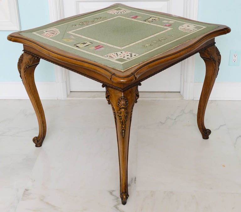 The top lined with trompe l'oeil needlepoint depicting a card game on a green ground. Very refined piece featuring double serpentine shape, ribbon carved frieze, shell carved cabriole legs terminating in scroll-form feet.