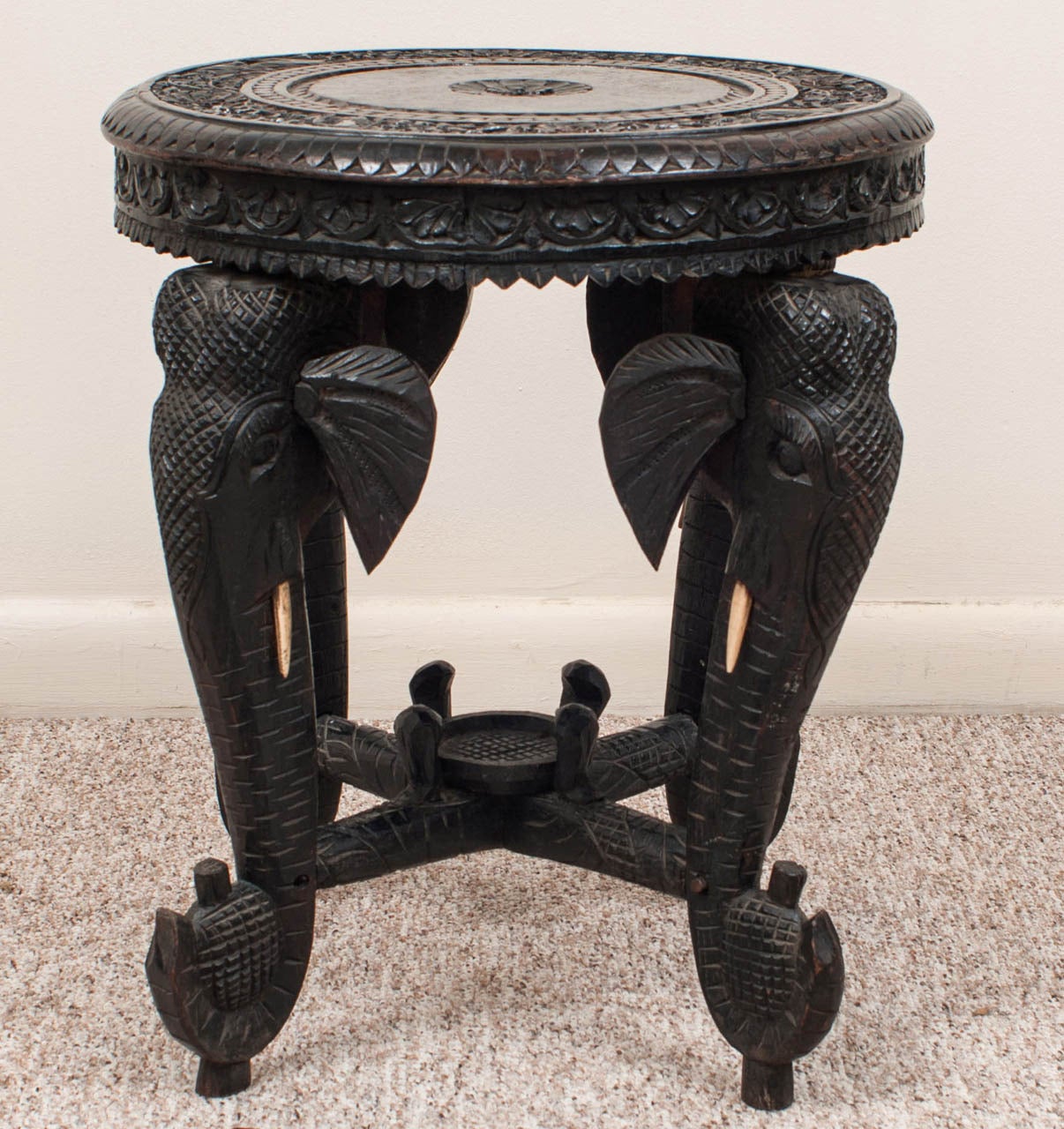 The round top supported by elephant form legs joined by a stretcher centered by a small platform for a vase or urn.