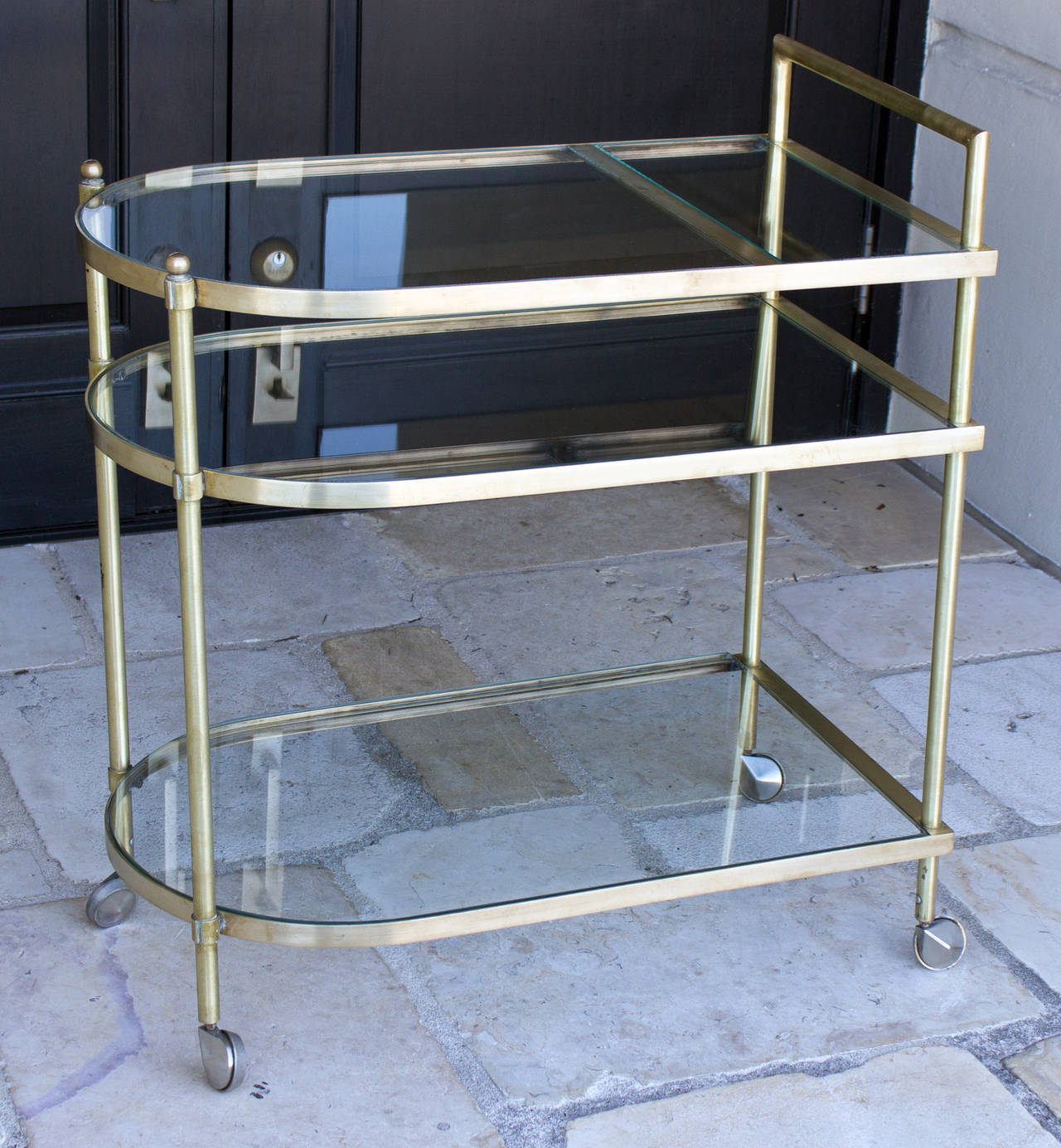 A brass bar cart with three glass shelves connected by vertical stiles, all raised on casters. The glass is newly replaced and the original finish has been polished,

 circa 1950. Dimension: Height: 33" Width: 29" Depth: 17".