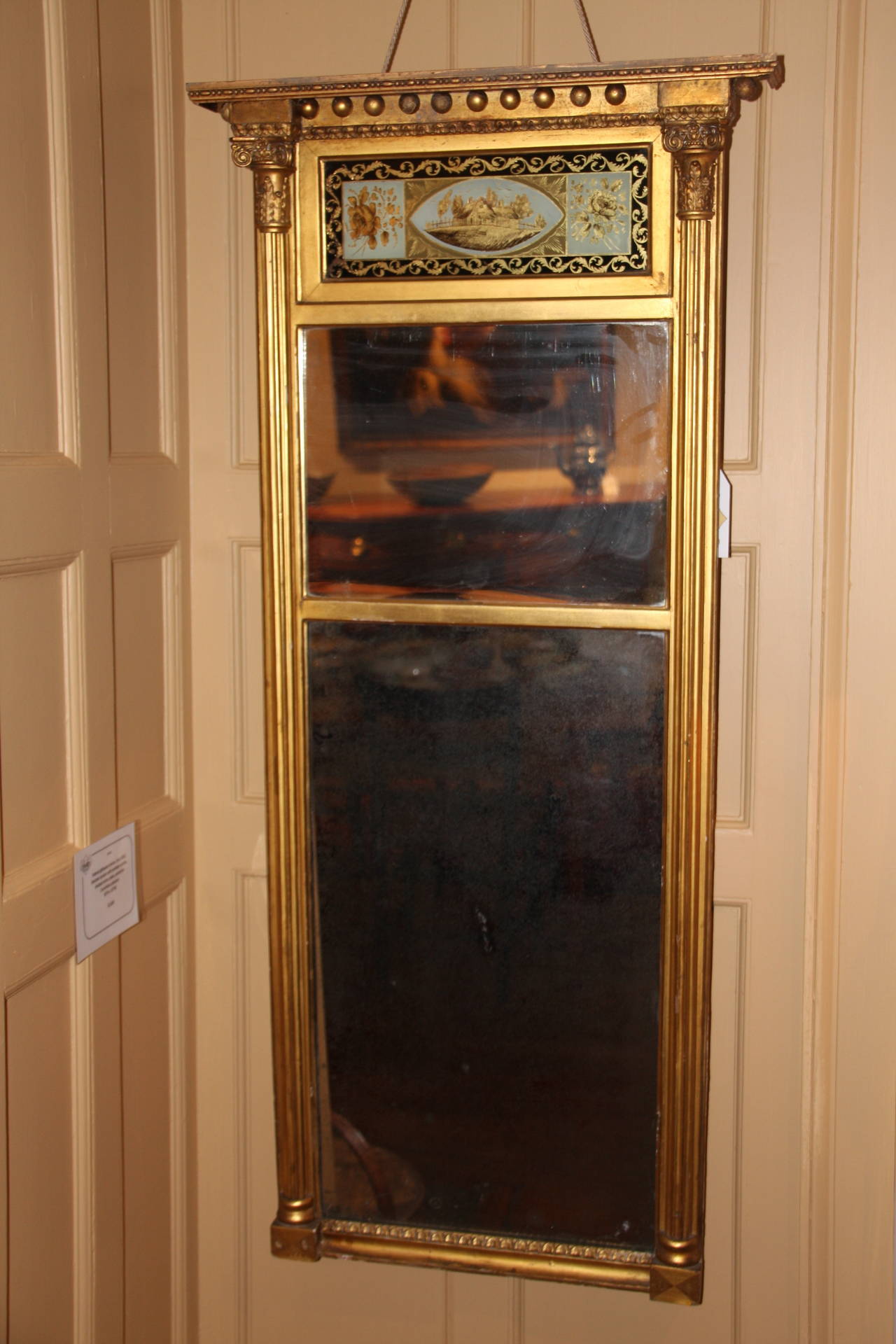 Federal giltwood mirror, circa 1815. Blocked cornice with pendant acorns above a frieze with floral and homestead scene. Divided mirror plate paired beneath Corinthian pilasters. One acorn missing.