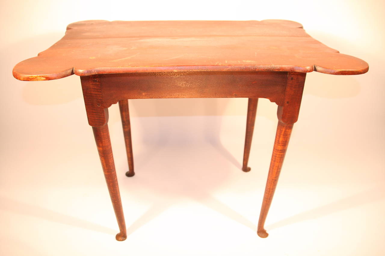 Queen Anne tiger maple tavern table, with a porringer top and turned legs supported by pad feet, retaining an old, dry red stain,  Expected surface wear and some alligatoring of paint.  

Circa 1760, Rhode Island.