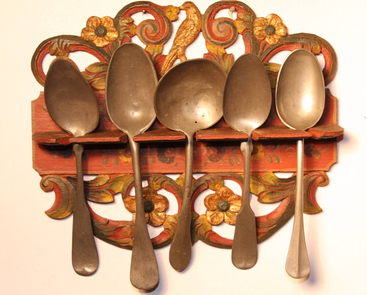 Wonderful, hand painted 19th-century hanging spoon rack with bird and floral decoration.  Red painted background with gold, green, and blue decoration.  Includes 5 pewter spoons from the early 19th century, some stamped OSV.