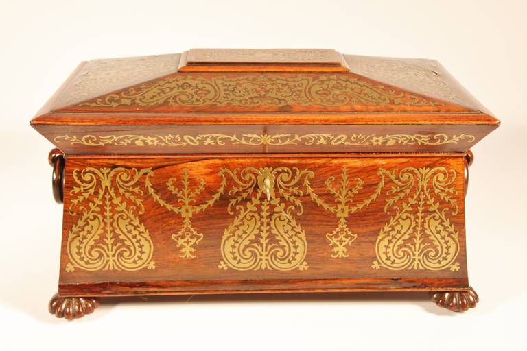 Beautiful sarcophagus shaped rosewood tea caddy with extensive brass inlay.  The interior is fitted with two hinged, lidded compartments for tea and velvet lined space for housing the original cut glass mixing bowl and sterling silver spoon. 
