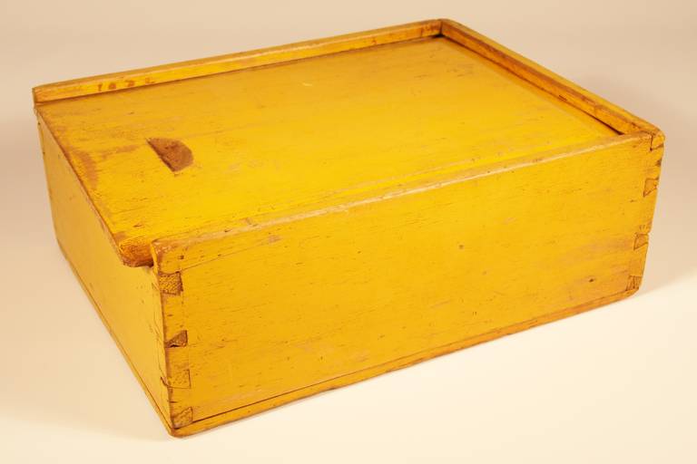 Fine slide top storage box in chrome yellow paint. Early 19th century New England with chamfered top and carved finger slot, having divided interior. Constructed of bass wood having wonderful consistent overall surface. Square nail and dovetail