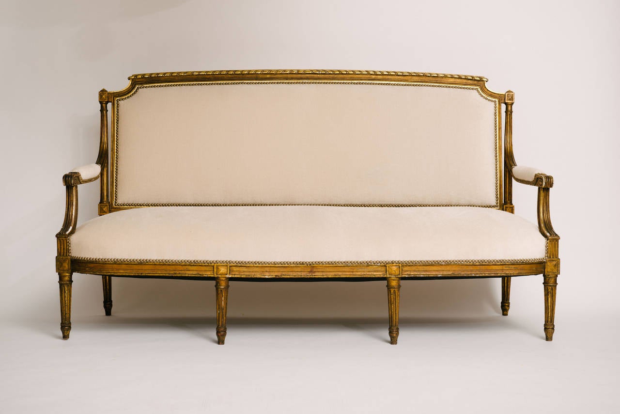 A Classic and stately 19th century Louis XVI giltwood canapé, newly upholstered in a creamy white ecru mohair silk velvet. Measures: 71.5