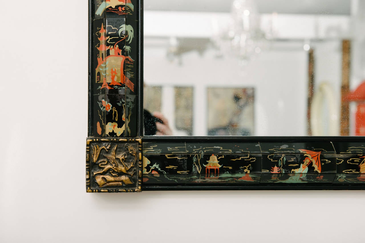 A black and polychrome Mid-Century Modern chinoiserie style églomisé mirror with carved wood corner detailing.