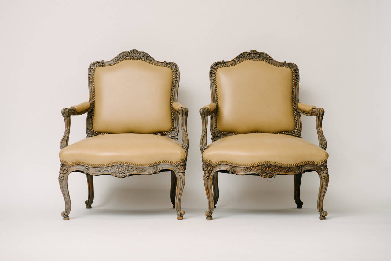 Pair of 19th Century painted and carved floral Louis XV fauteuils newly upholstered in palomino leather with nailhead detail.