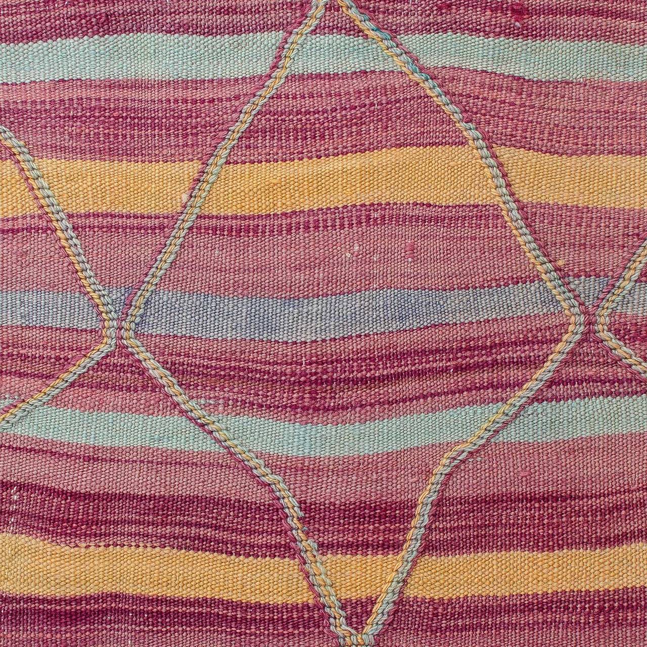 A Talsint hanbel (flat-weave) from the Ait Bou Ichaouen tribe with a woven lozenge network raised slightly above the surface, creating a textural chainlike effect overlaying the striped field. Colorful palette includes magenta or purple, and pale