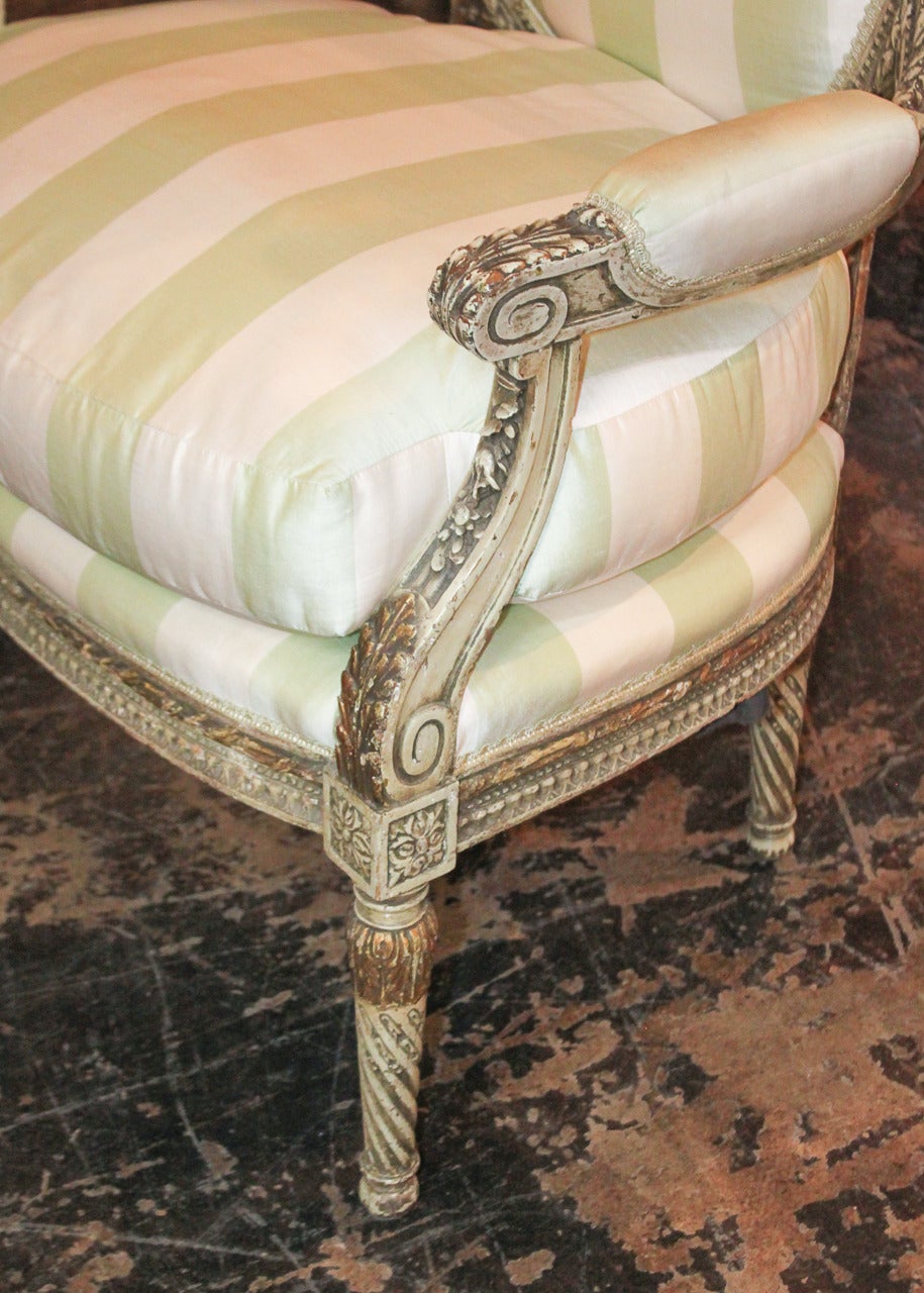 Alluring pair of French Louis XVI painted and parcel-gilt fauteuils. Having lovely hand-carved frame adorned with ribbon and acanthus leaf motif and resting on tapered spiral fluted legs. 