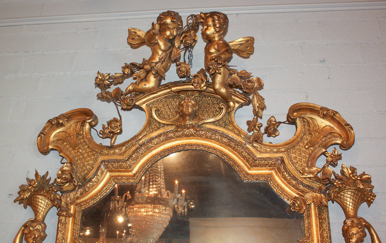 Monumental palace size French Louis XV figural hand-carved mirror.  Having large carved wood and gesso winged putti surmount, side mounted figural carytids, original mirrored glass, and all in original lustrous gold gilt finish.  A rare classic of