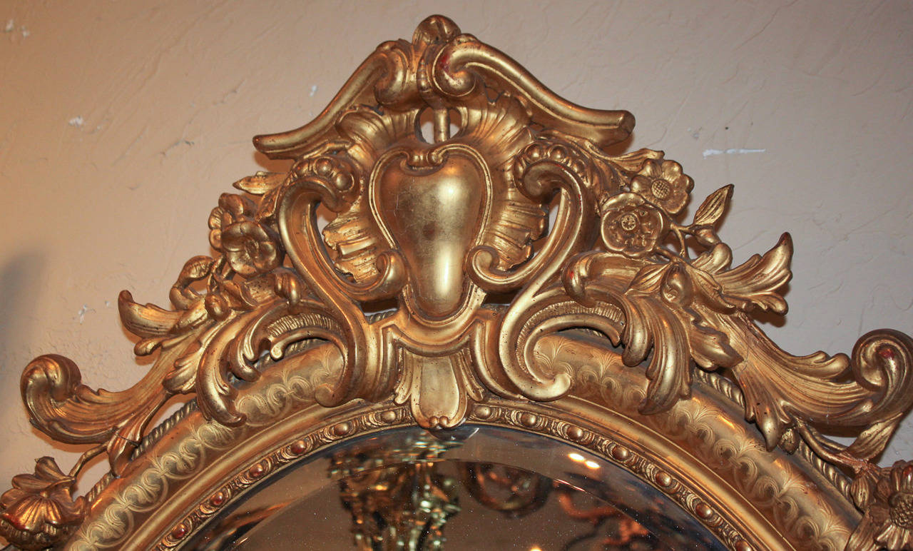 Exceptionally detailed French Louis XV mirror with oval beveled glass. Having elaborately hand-carved cartouche in acanthus leaf motif, lined in egg and dart beading, and a beautiful gilt finish. Please view all pictures to enjoy.