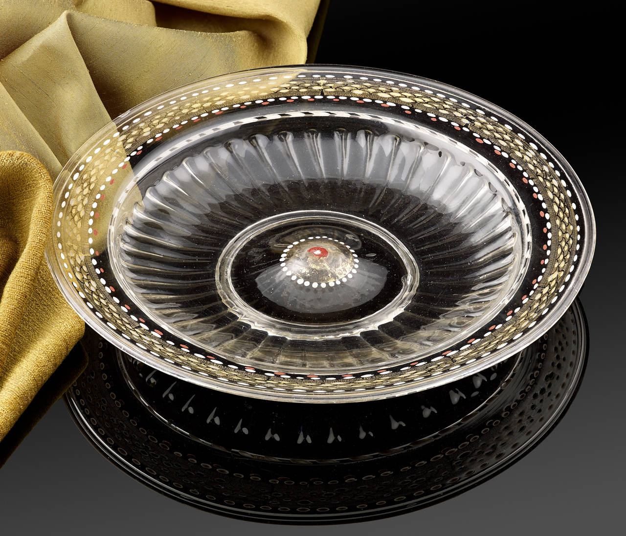 A Very Rare Venetian low footed Glass Bowl, C.1500 - 1525; The shallow tray of the bowl moulded with a series of ribs radiating from the raised centre; the broad rim decorated with an intricate pattern of gilded scales embellished with white, red