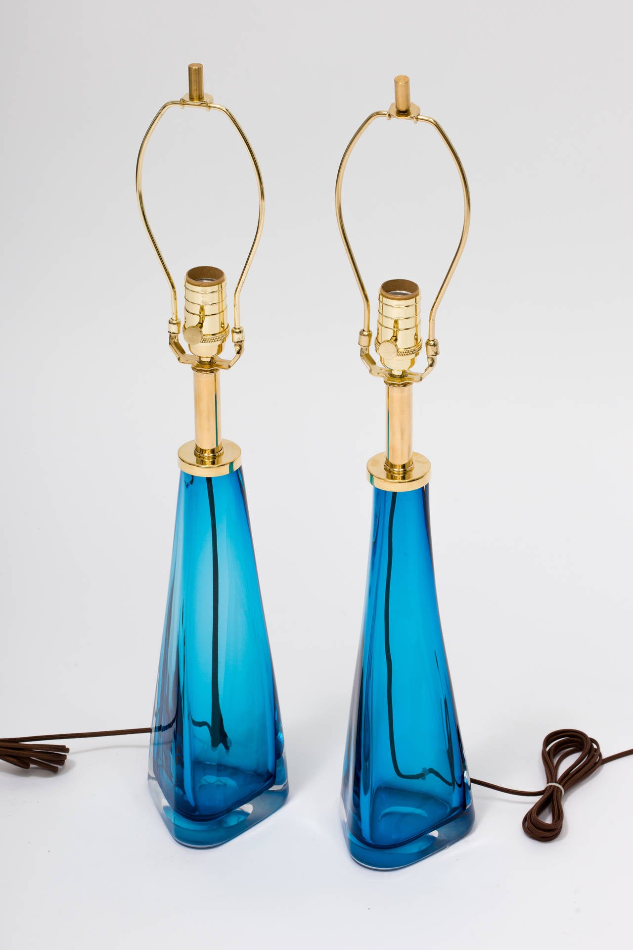 A pair of blue glass lamps with thick clear glass casing with brass hardware in the Manner of Nils Landberg for Orrefors
These are made to order.