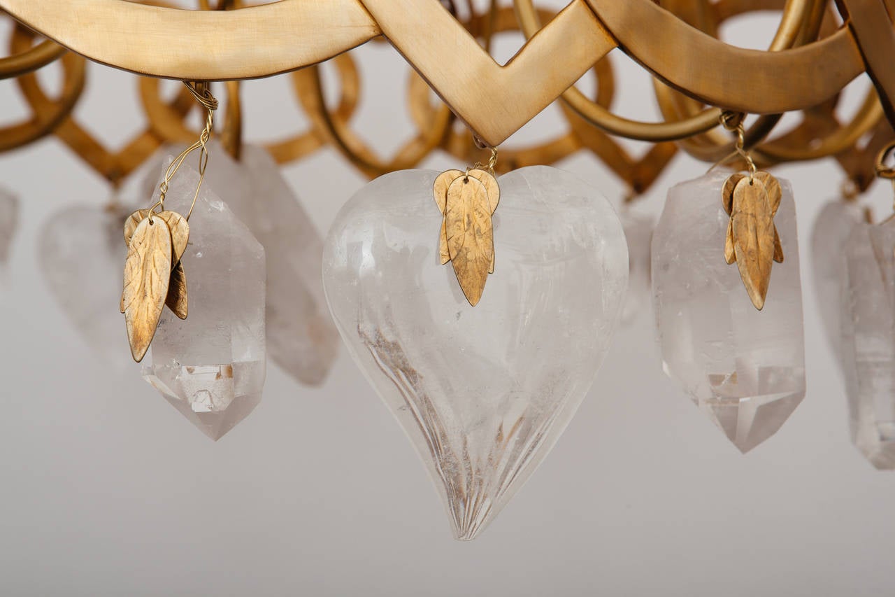 Refined chandelier in gilt bronze with rock crystal drops
The body is formed from a band of interlinked hearts and ovals issuing hand carved rock crystal hearts and natural quartz pendants with foliate mounts suspended from a conforming corona by