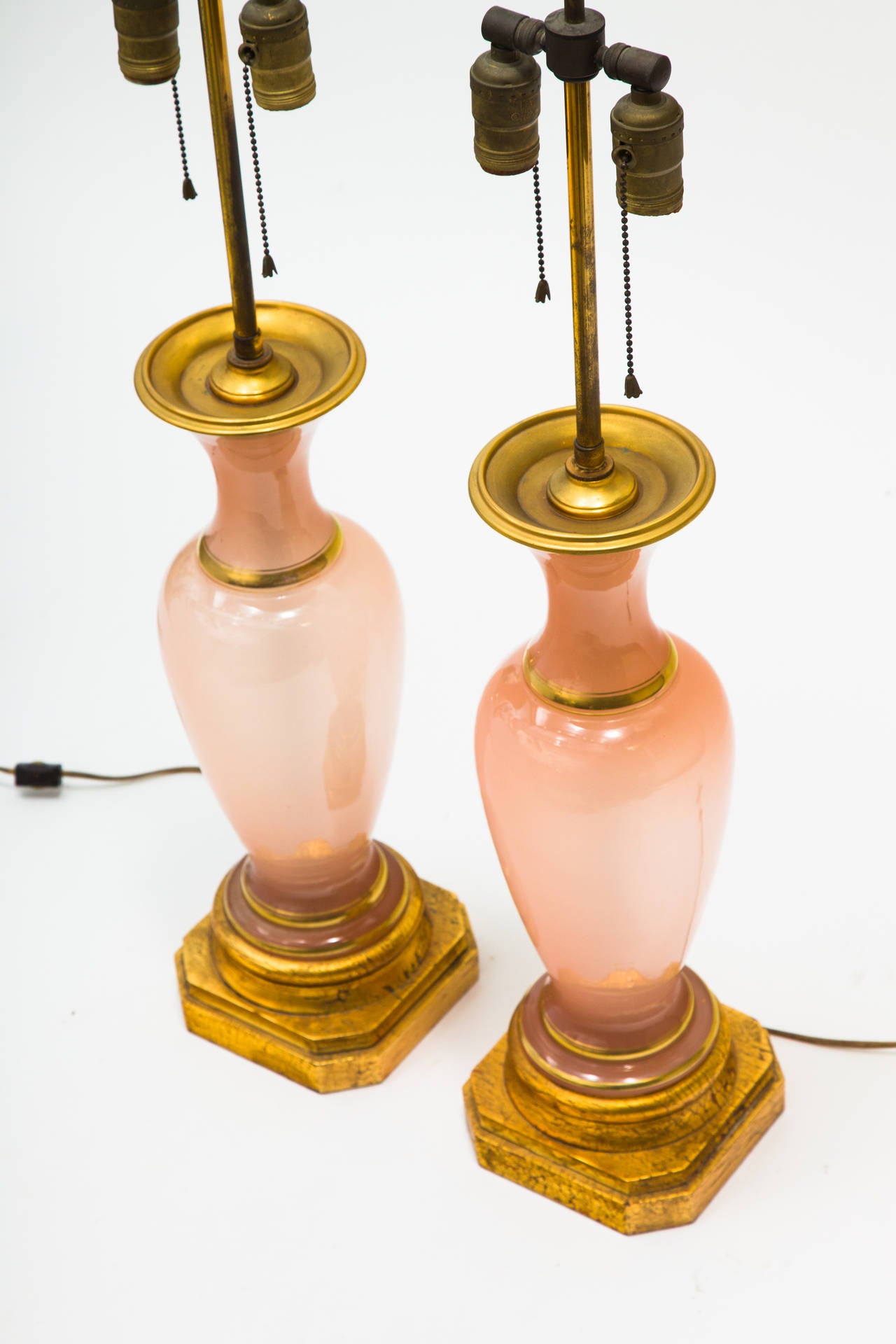 Pair of peach colored opaline table lamps on wood gilt bases with gilt accents. One lamp is lighter in color than the other.

 