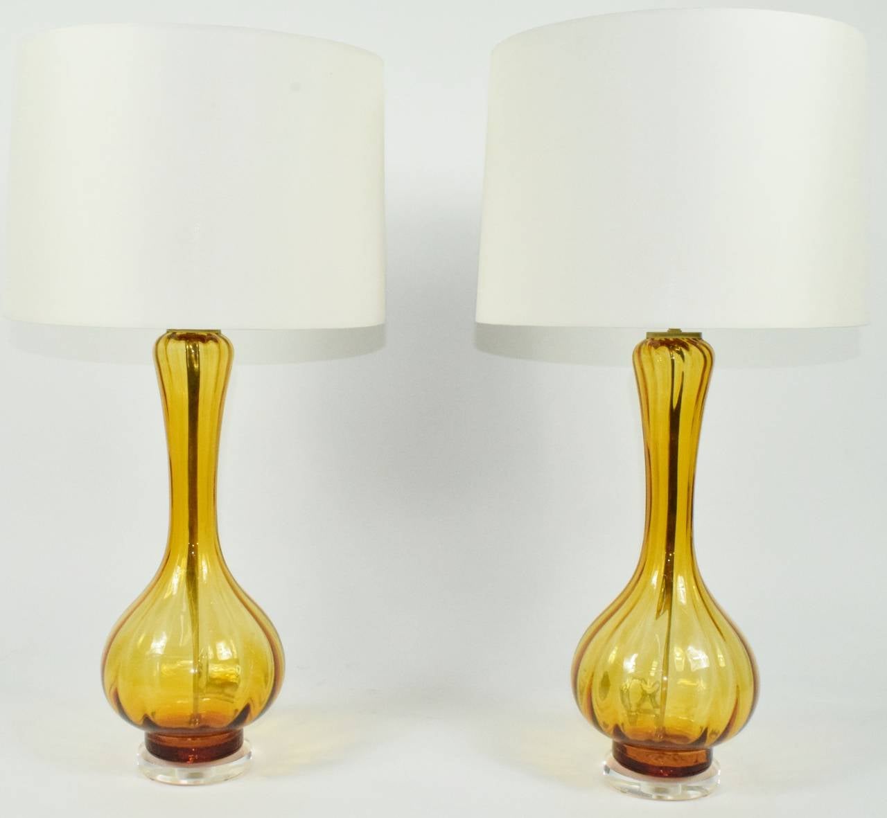 A beautiful pair of Empoli Italian optic glass lamps in a vibrant orange/gold. The lamps are a teardrop form with vertical optic stripes and sit on a lucite base. They have been completely rewired with new brass fittings. The socket can utilize a