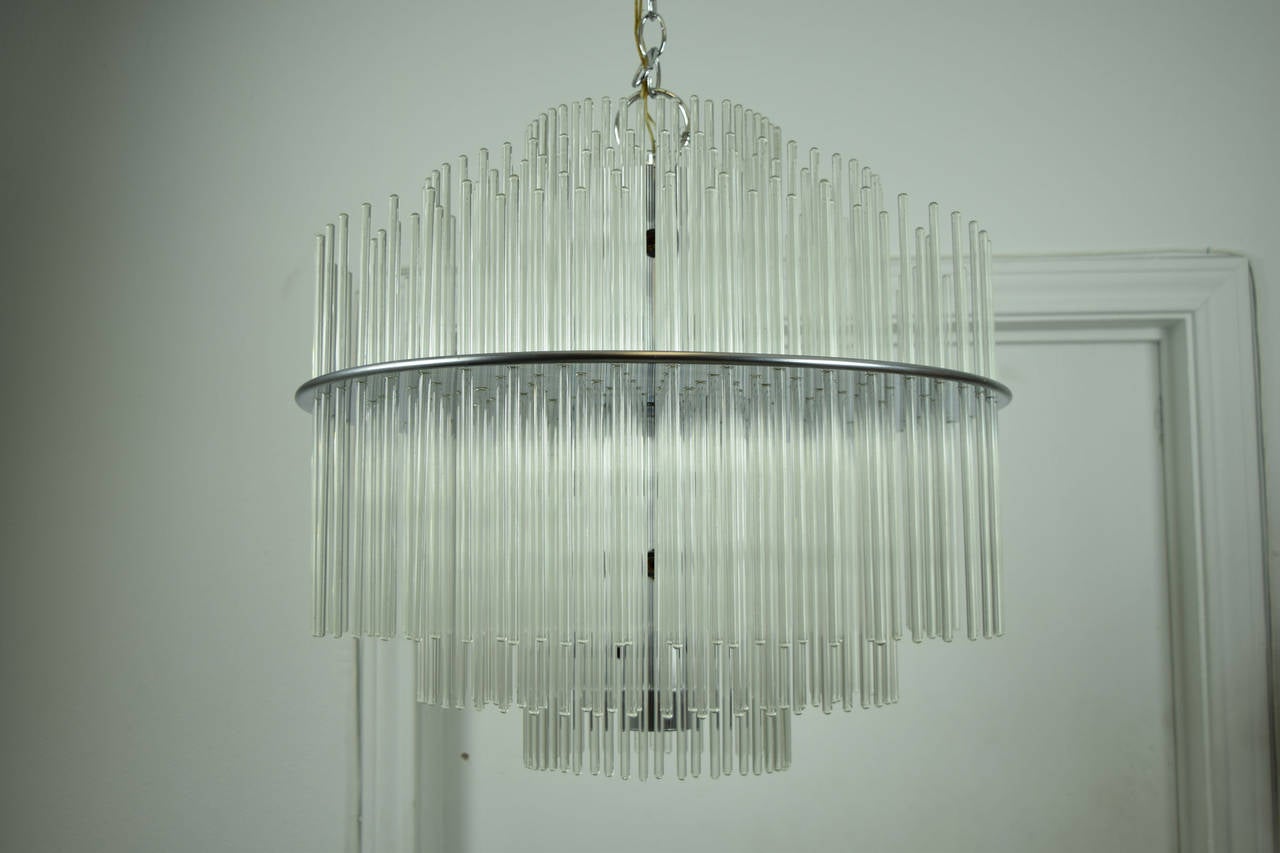 This chandelier has over 240 glass rods and is in perfect condition. There are five circles of glass rods with three different sizes. The largest glass rods measure 22 inches. The Lightolier label is intact on the chrome disc that holds the glass