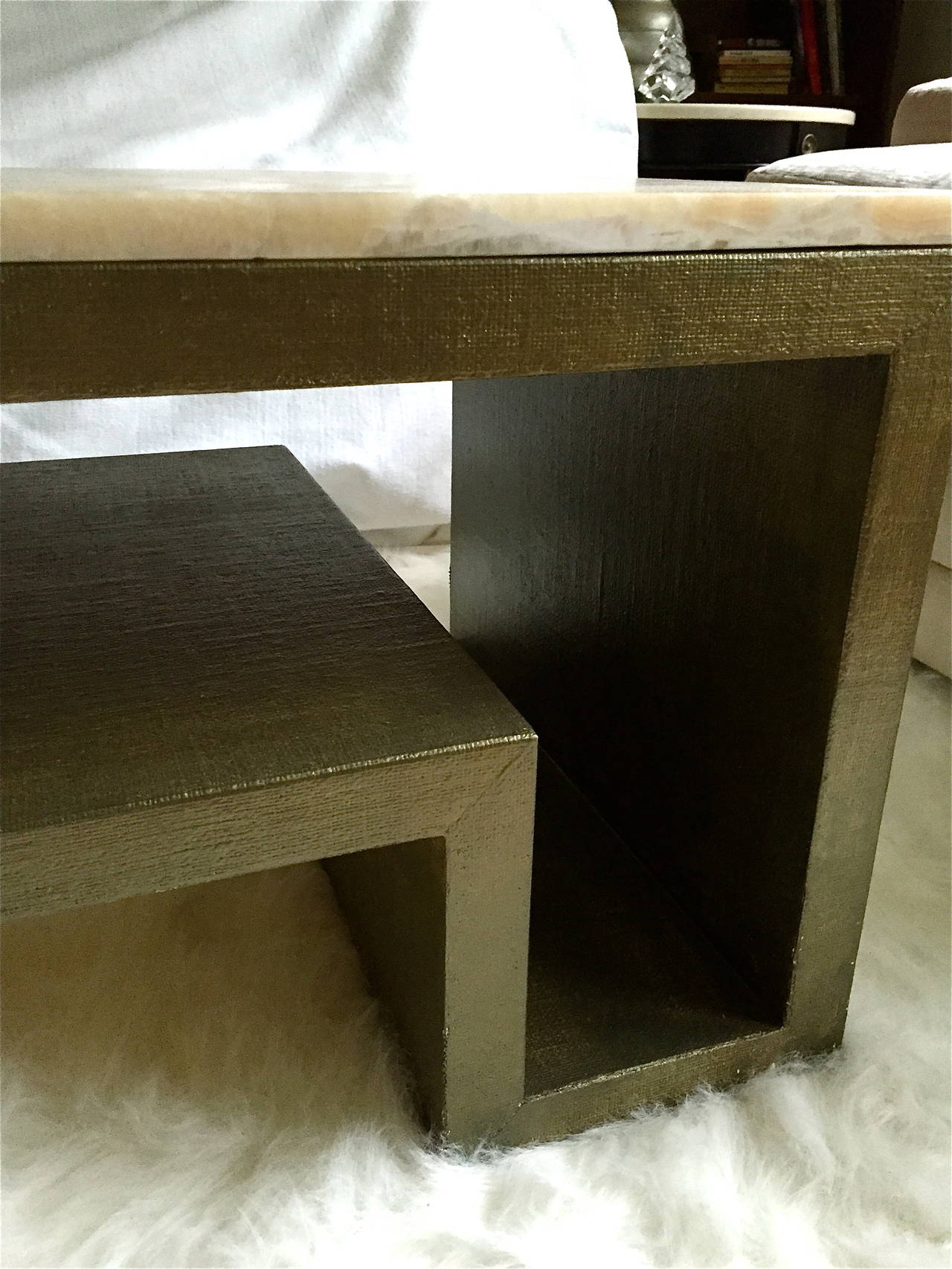 This coffee or cocktail table is linen-wrapped and painted in a moss green with a faint metallic finish. It has a highly figured onyx top. The base is wood, which is wrapped in linen. It measures 44