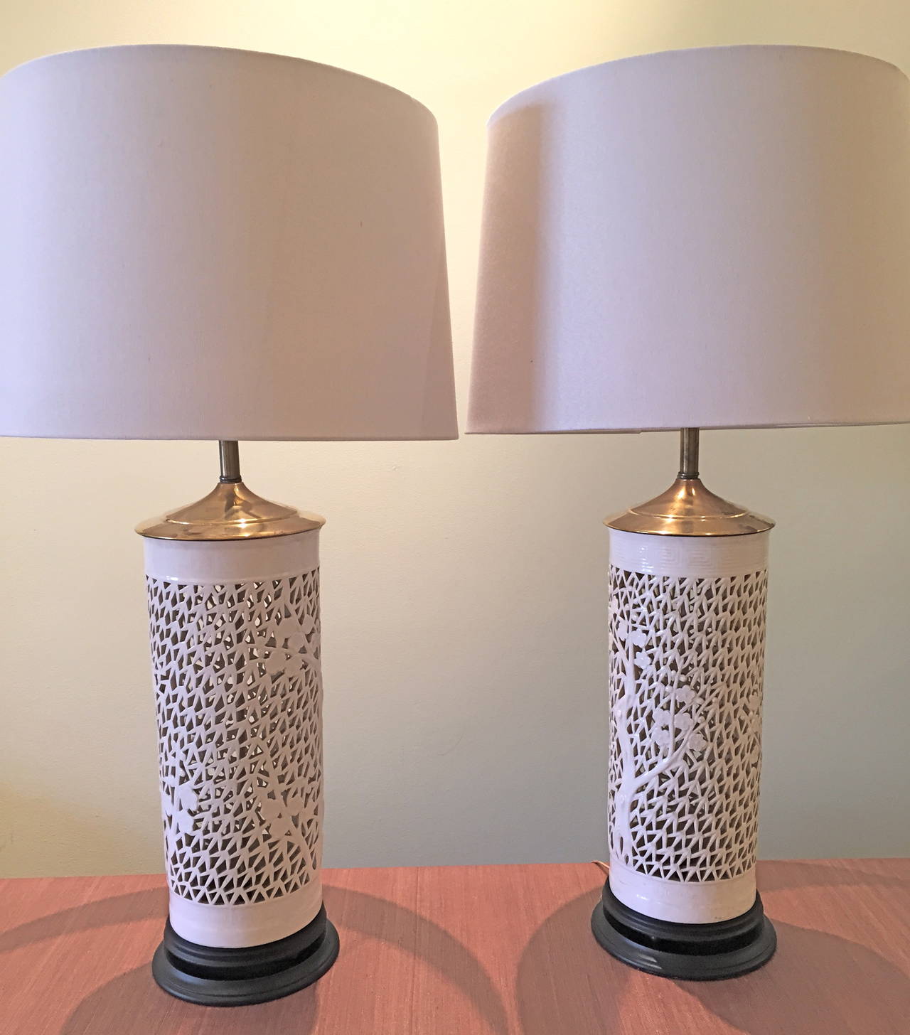 This graceful pair of lamps features a stylized motif of trees and branches in relief against a background of open fretwork.  They are 26.5 inches to the top of the finial.  The porcelain body and the stand are 18.25 inches high.  The shades are not