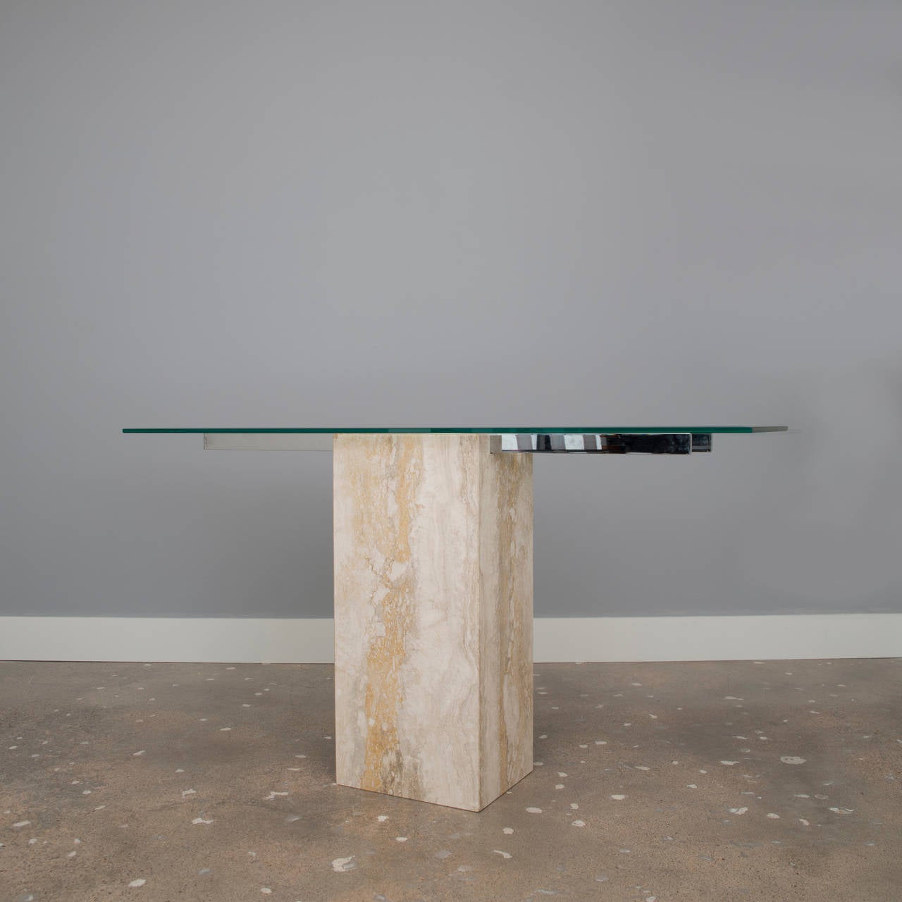 This elegant console table by Ello has a base of Italian travertine marble and a pair of nickel-plated arms which supports a glass top. Sleek and Minimalist.