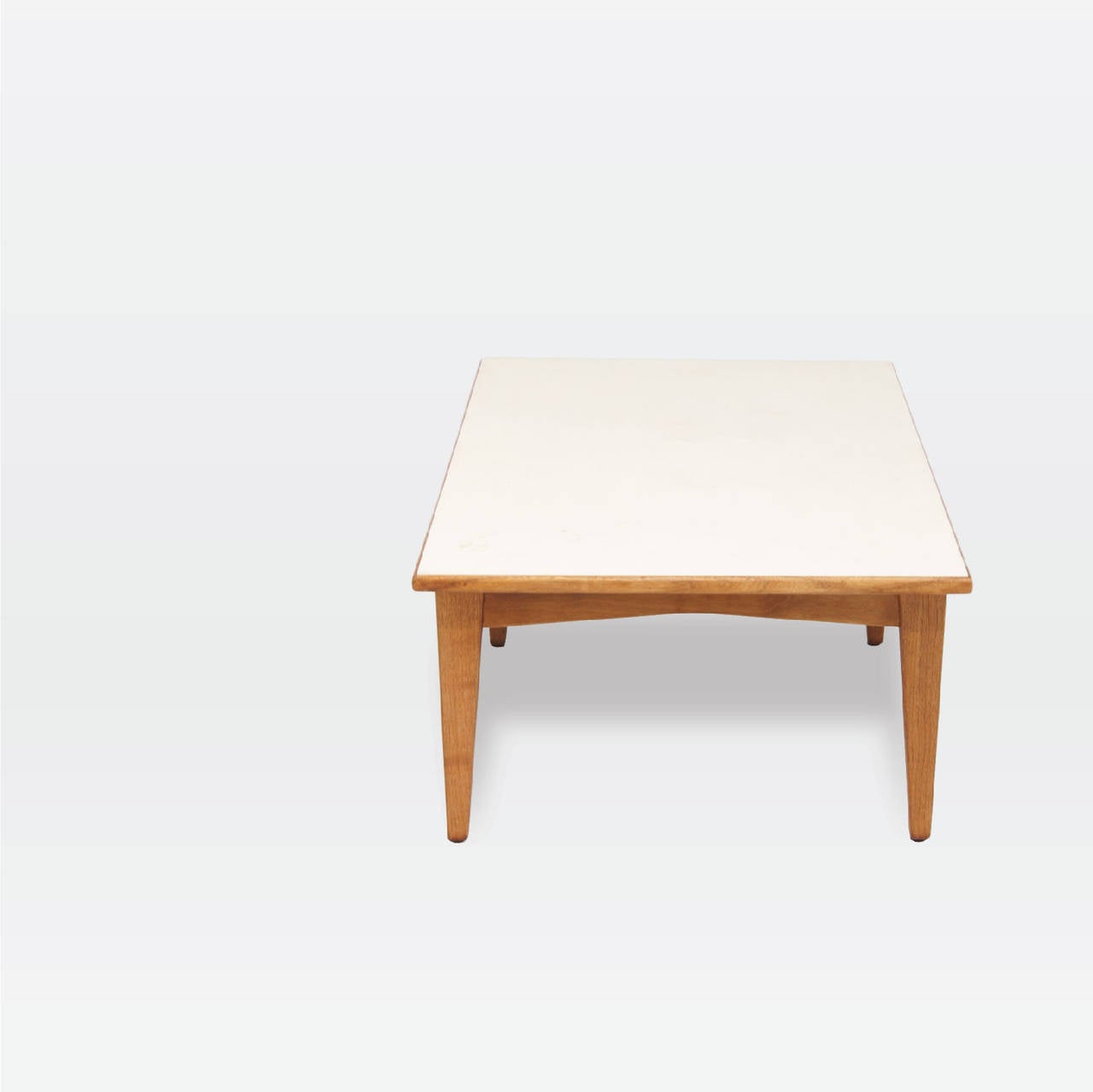 An occasional table in solid walnut featuring four tapered legs supporting a floating rectangular white laminate top.