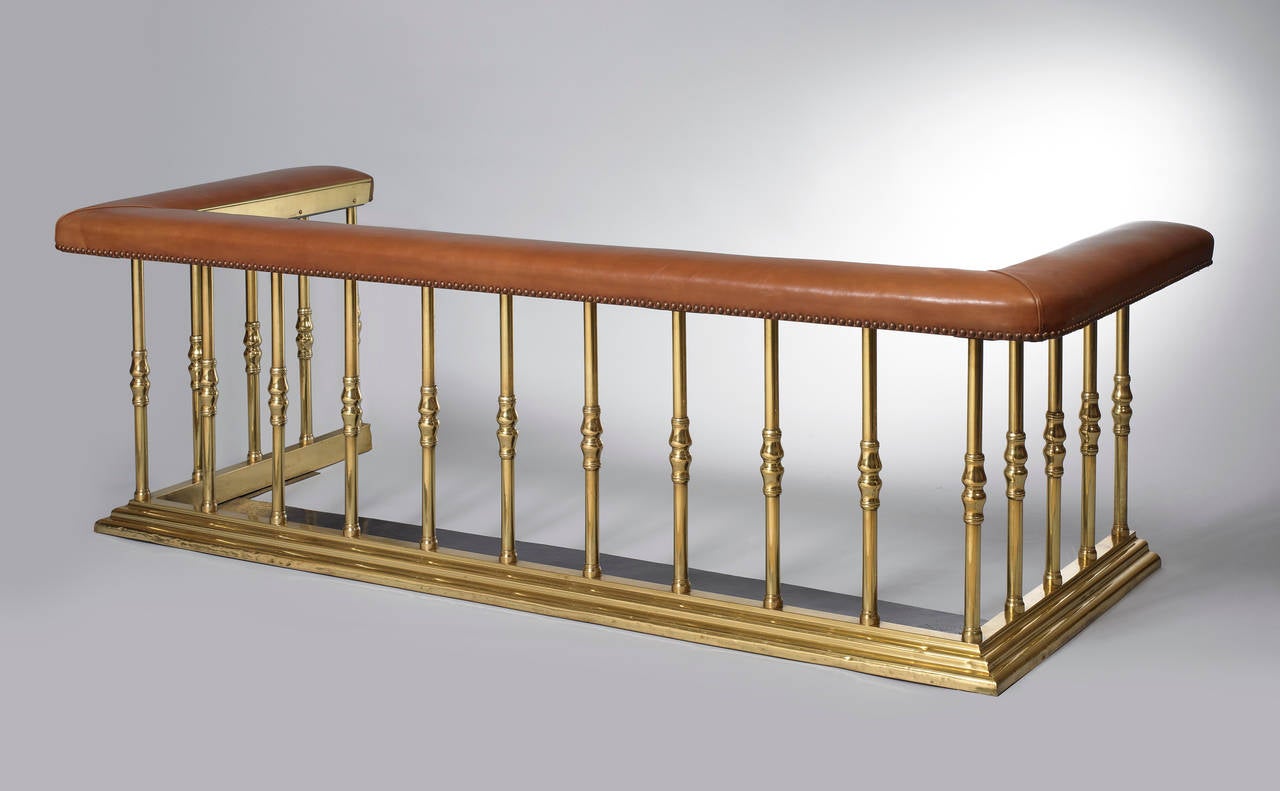 An English brass and leather upholstered club fender, mid 19th century.  The tan leather padded rail on tubular supports, with baluster knops on a stepped plinth.

Provenance: Estate of Henry Ford II