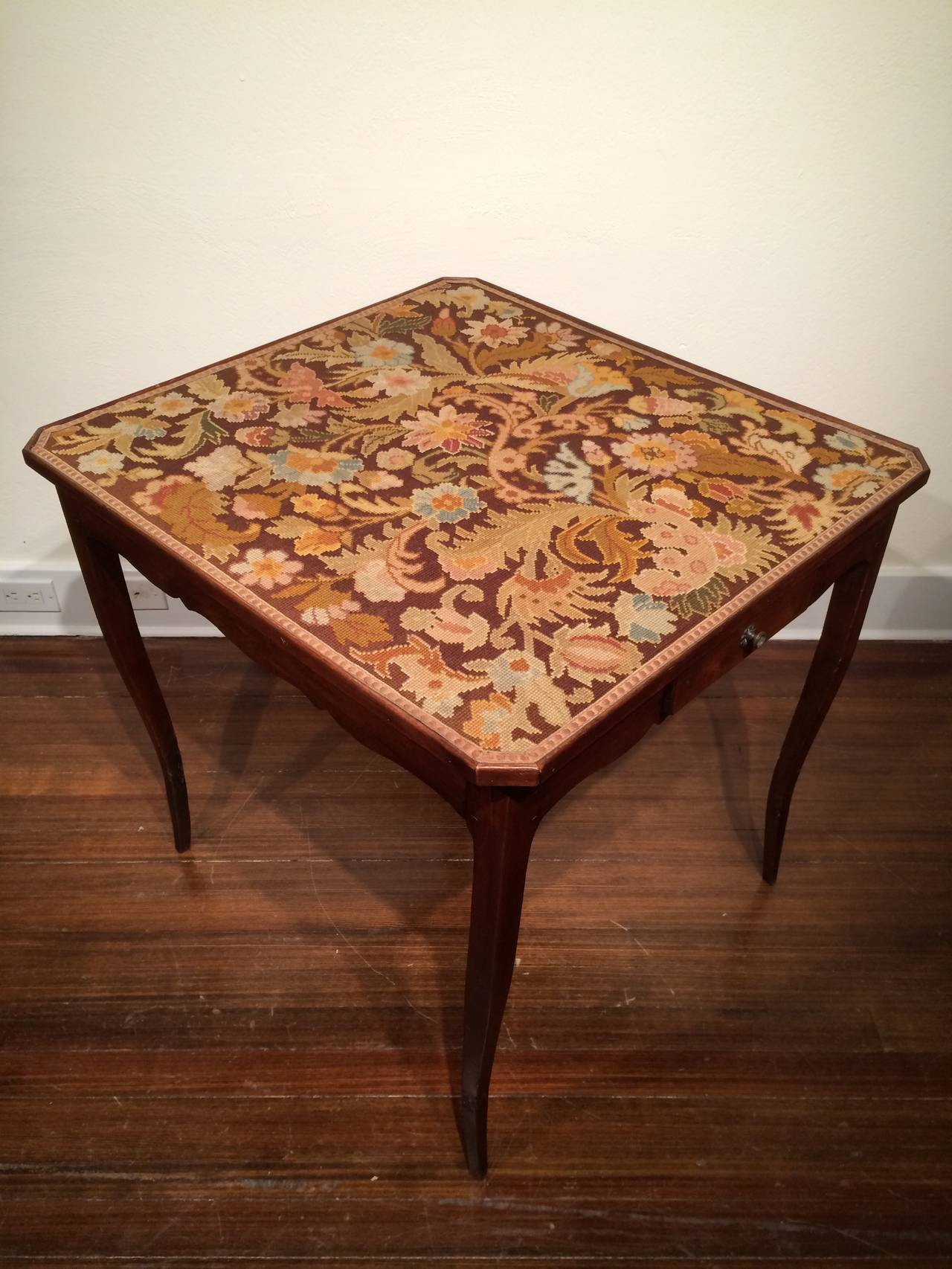 Needlework inset surface on a rectangular top with clipped corners above a scalloped apron with a single drawer on two sides raised on cabriole legs.
France, 18th century.