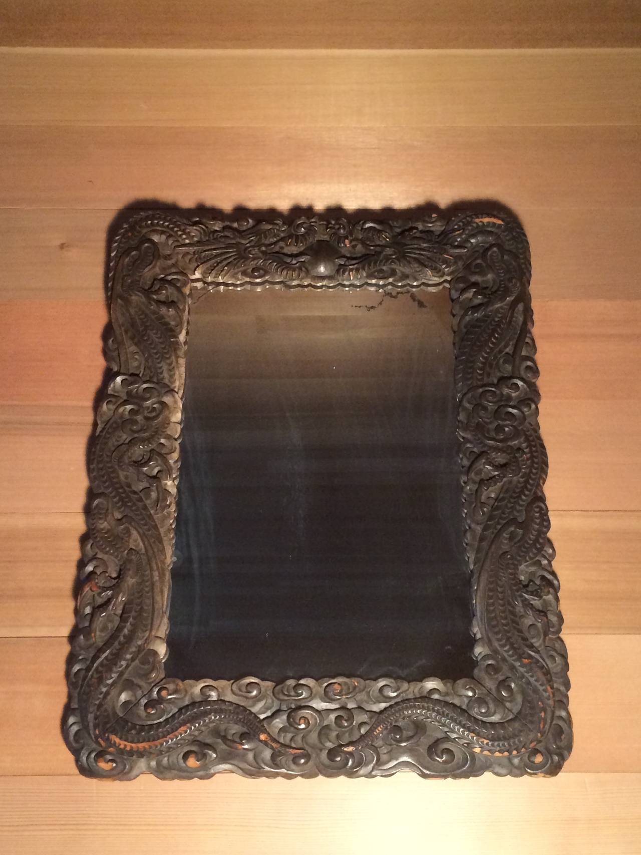 In China dragons are a symbol of authority and good fortune. This framed mirror features a pair of dragons chasing the flaming pearl of wisdom and truth above swirling clouds. 

Carved and stained wood with original antique mirror. 
circa 1890.