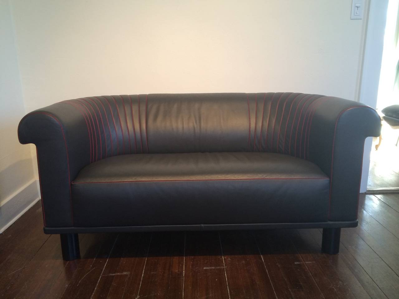 In the spirit of Charlotte Perriand, Black leather with red leather piping raised on ebonized wood cylindrical feet.