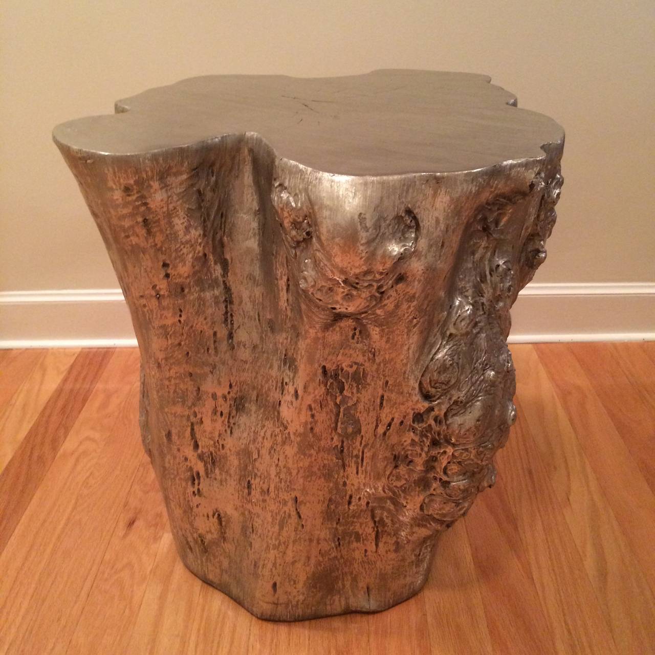 A large silvered composite mold of a tree trunk, used as a side table.

