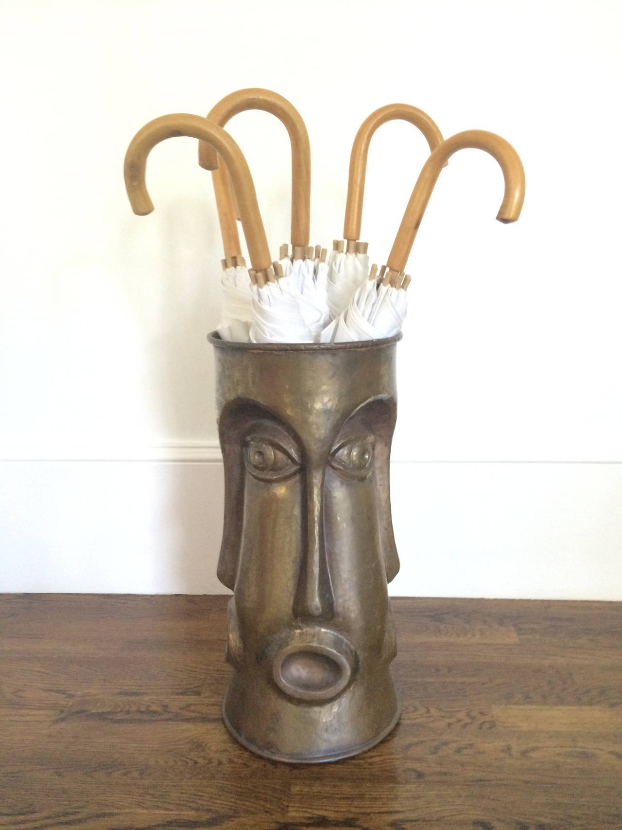 An Italian brass umbrella stand with repeating face motif. Hand hammered seamless cylinder, circa 1960's. Stamped 