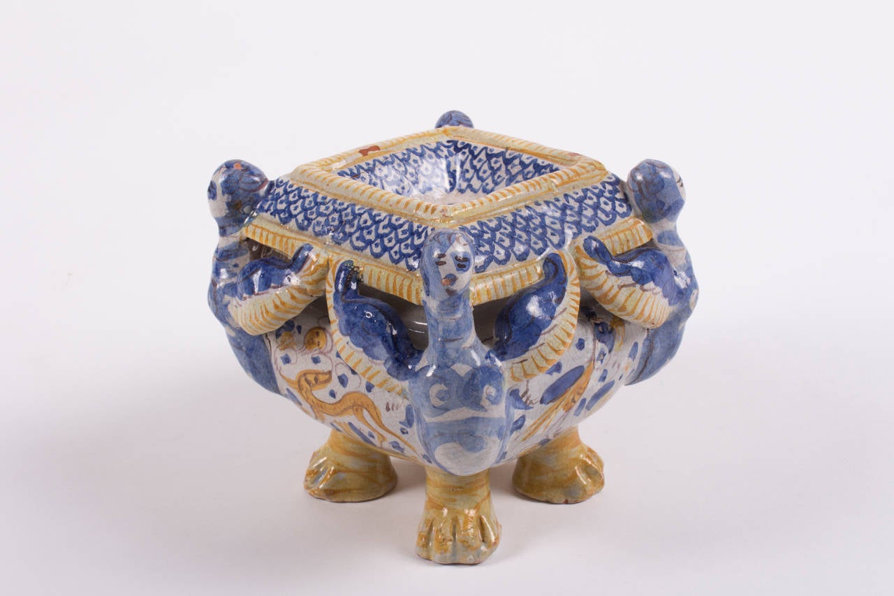 A powerful polychrome majolica saltcellar (Saliera)  with four caryatid lions with wings, standing on four lion paws. Roundly decorated with mythological fabulous creatures, grotesque and grimaces;  in the centre an angel head. A beautiful and rare