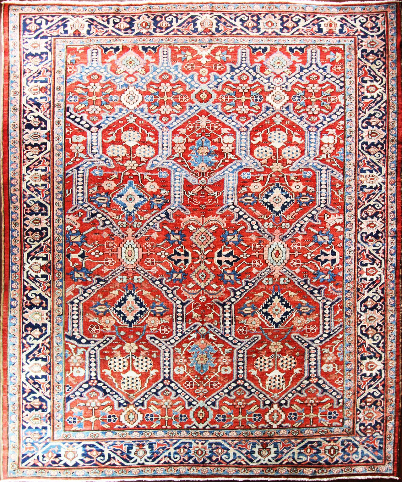 The madder red field with unusual all-over design featuring bold poly chrome palmettos linked in a trellis by blue dragon-like motifs, all within a wide deep blue flower-head and leaf main border. This rug consist of central medallions surrounded by