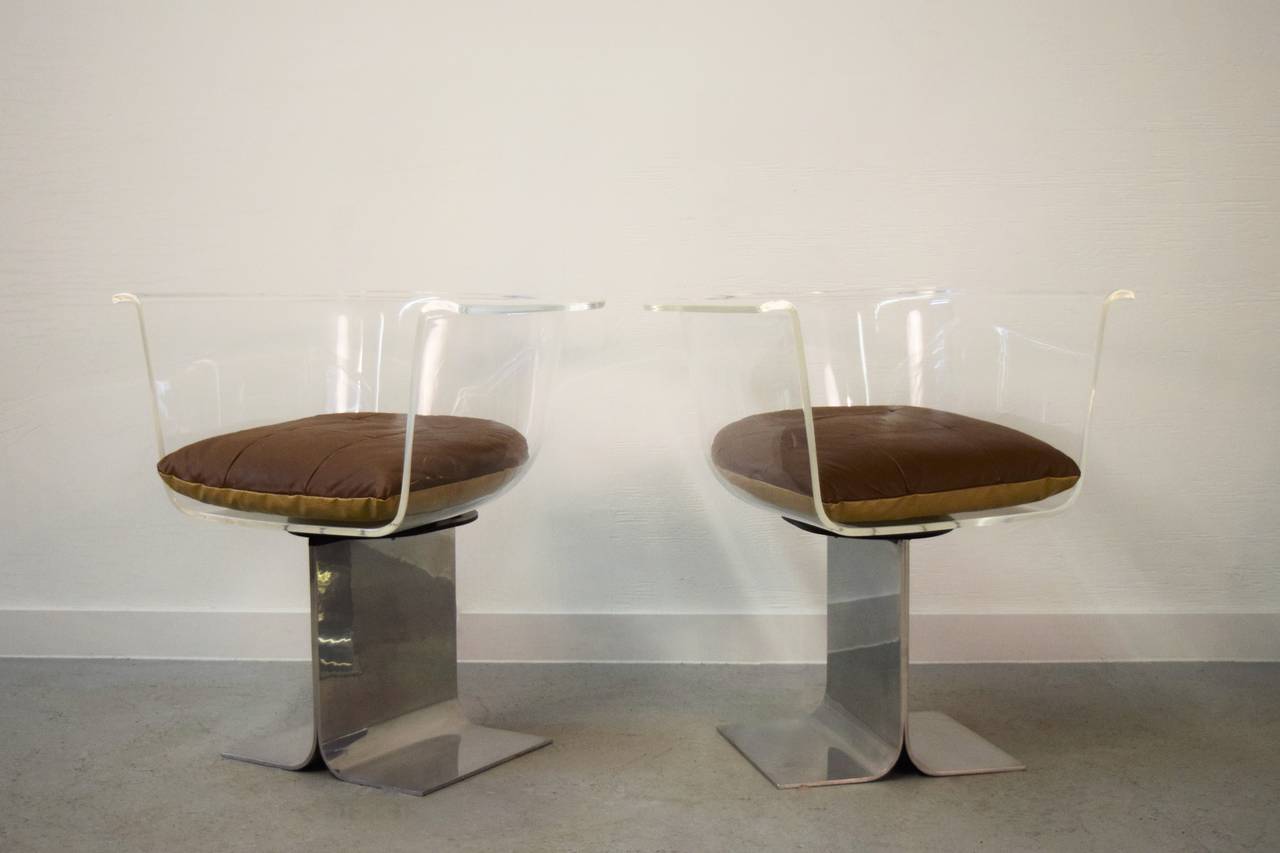 Lucite chairs swivel left to right with polished steel bases.