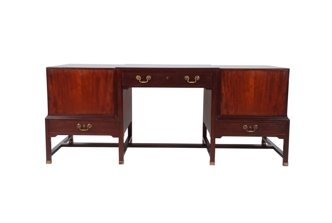 Kaare Klint unique Cuban mahogany desk on eight-legged frame with brass shoes. Side sections with fold-down leaves on front, interior with five trays, front with three drawers. Handels of brass. Top divided into three sections, middle section