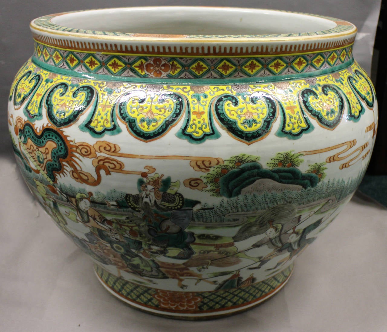 A large Chinese famille vetre fish bowl decorated with a geometric patterned border and a large wraparound scene of warriors on horseback, large goldfish swimming through weeds decorate the inside.

(Buyers in the UK and Europe will be subject to