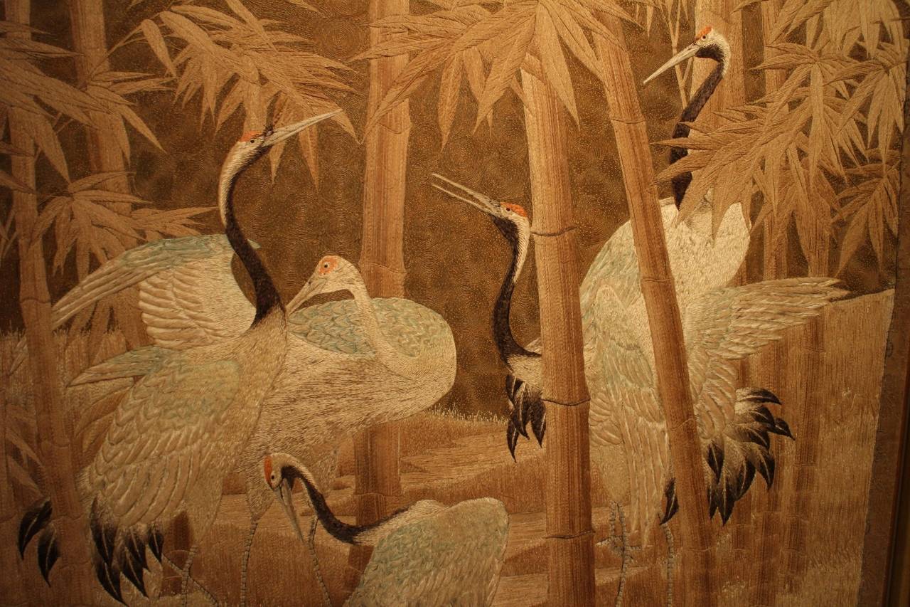 A large framed Japanese silk embroidery of red crowned cranes in a bamboo forest.