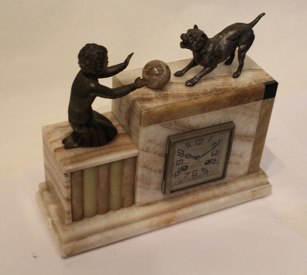 The marble case has wonderful contrasting colours with the figure of a young girl rolling a ball to her pet dog. The square dial showing Arabic numerals and Hebert's signature and town of work.

This Art Deco piece has an eight day movement which