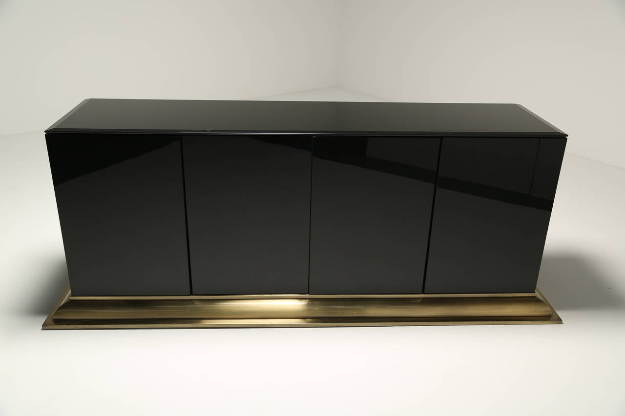 A Black Glass 4 door Sideboard on stepped brass base by Ello furniture, circa 1970. A Very elegant sideboard in excellent condition with a lovely brass stepped base that will look great in any interior. Perfect for a home setting or as an office