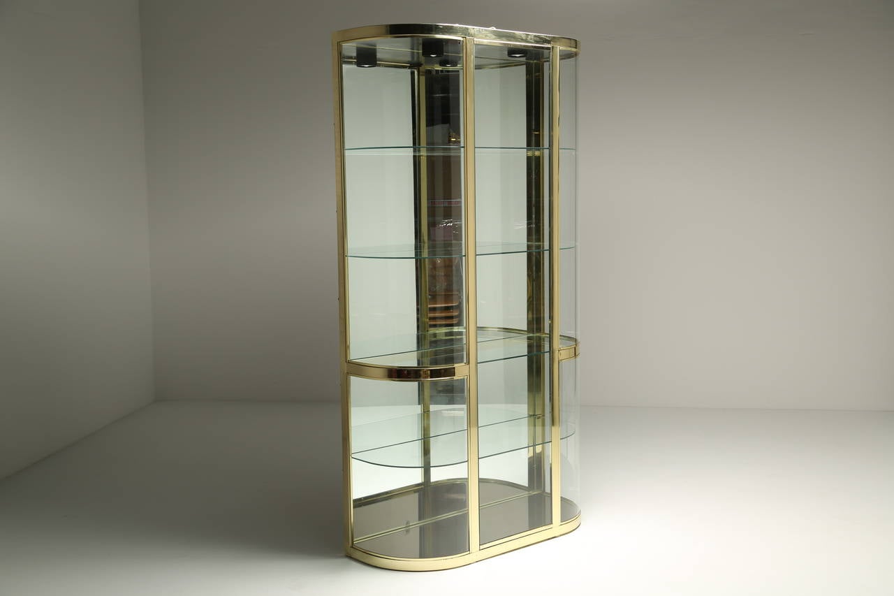 A curved glass vitrine / display case with 5 internal shelves and two down lighters all in a beautiful brass cabinet. A great unit that would suit either a home or a business setting. Ideal for displaying products or your favourite objects.